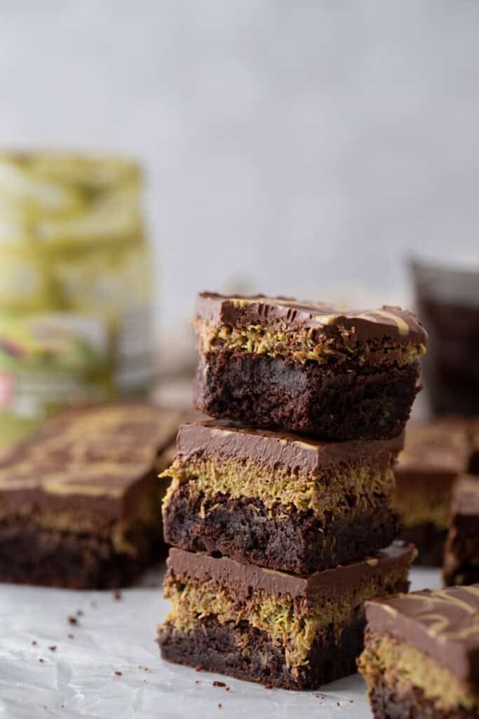 Stack of three Dubai chocolate brownies showing the pistachio kunafa layer between a fudgy brownie base and thick chocolate ganache topping