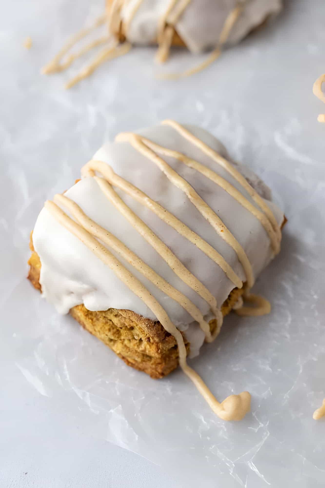 Glazed Starbucks pumpkin scone copycat with white icing and a pumpkin spice drizzle on top.