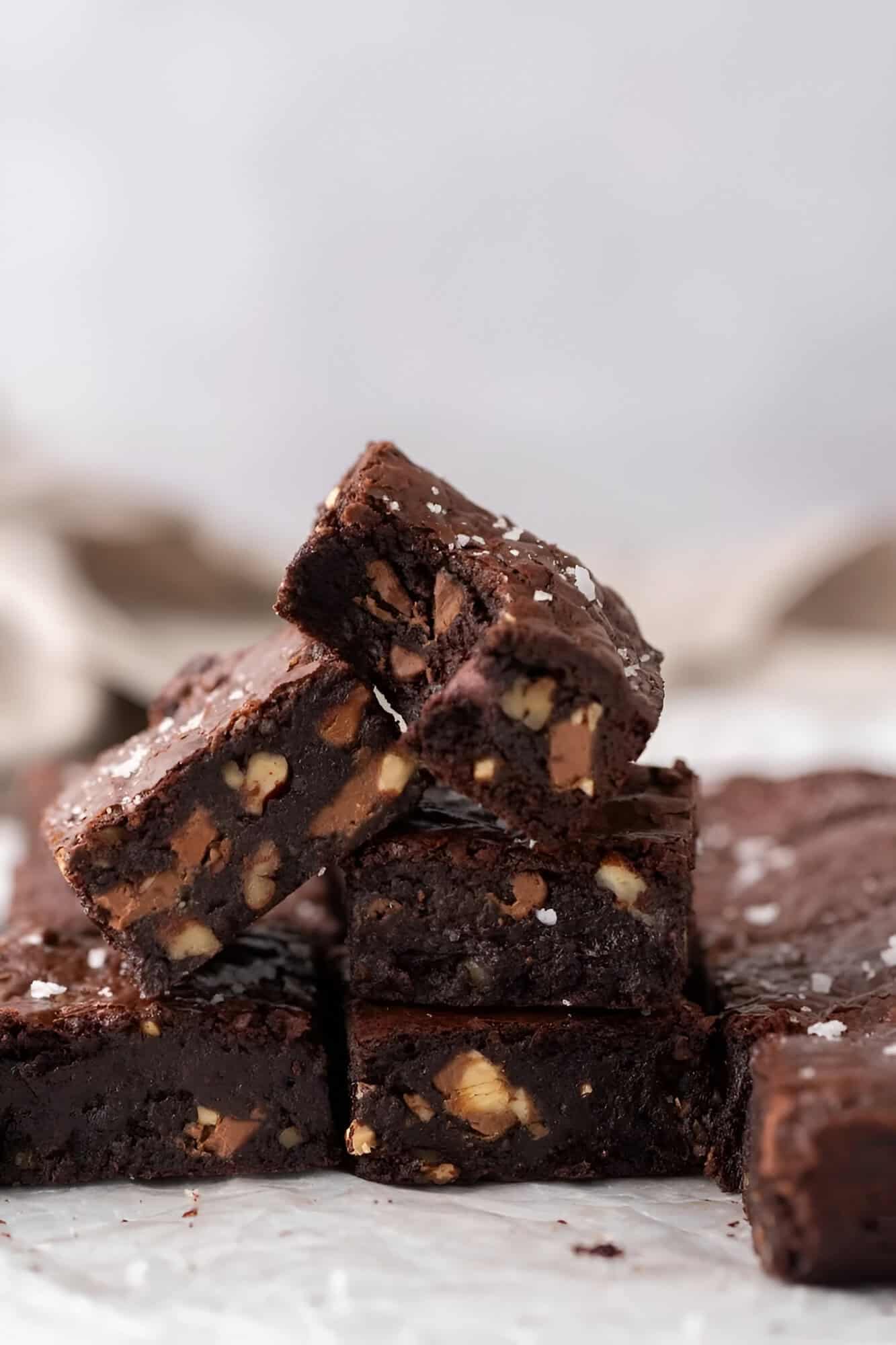 Nine squares of fudgy brownies with shiny crackly tops and flaky salt on parchment.
