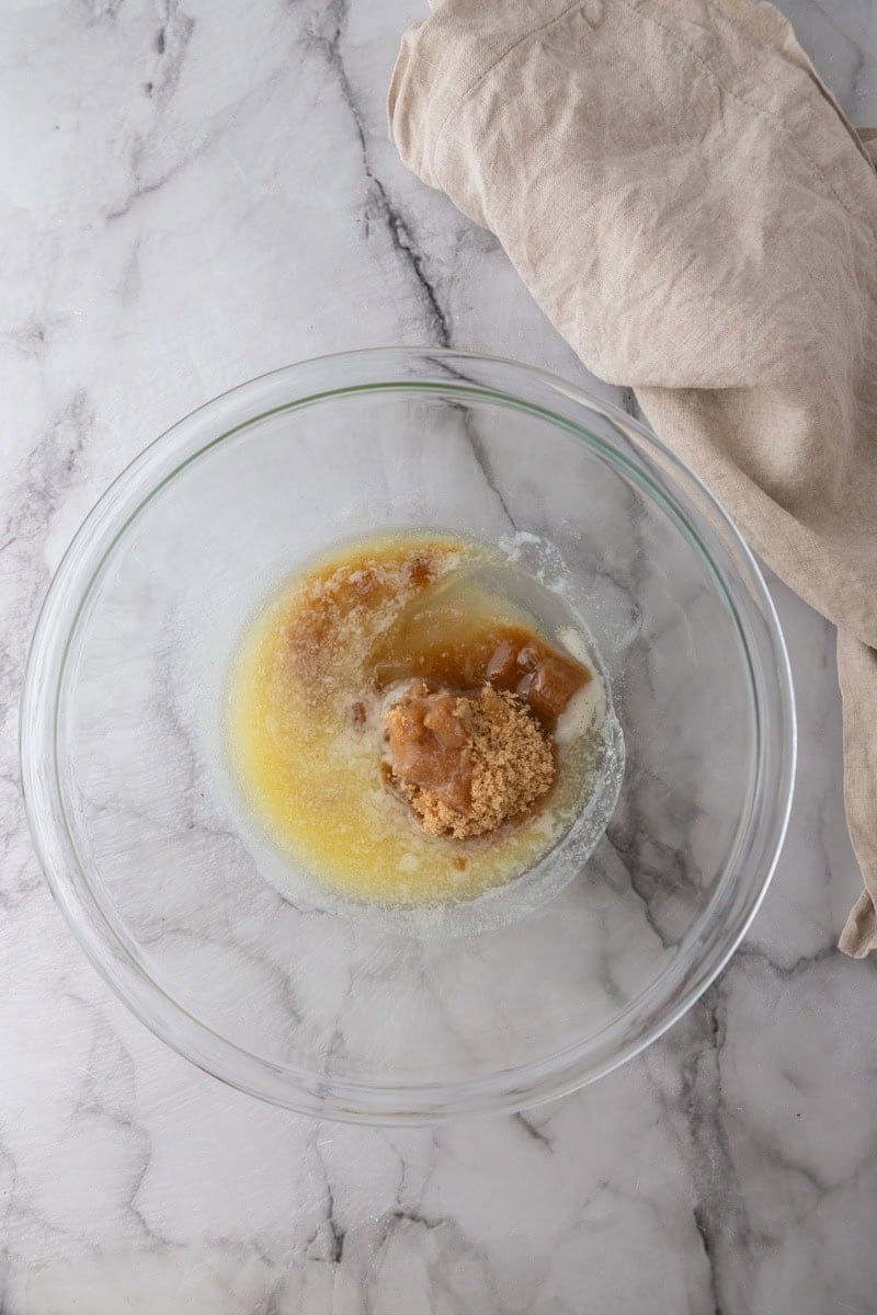Melted butter, brown sugar, and sugar in a glass bowl for chocolate chip cookie cake.