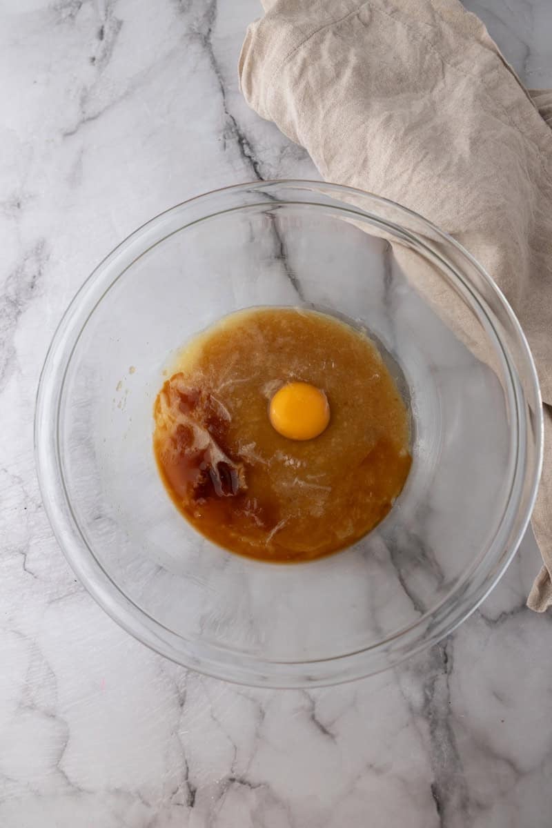An egg and vanilla added to the butter and sugar mixture in a glass bowl.