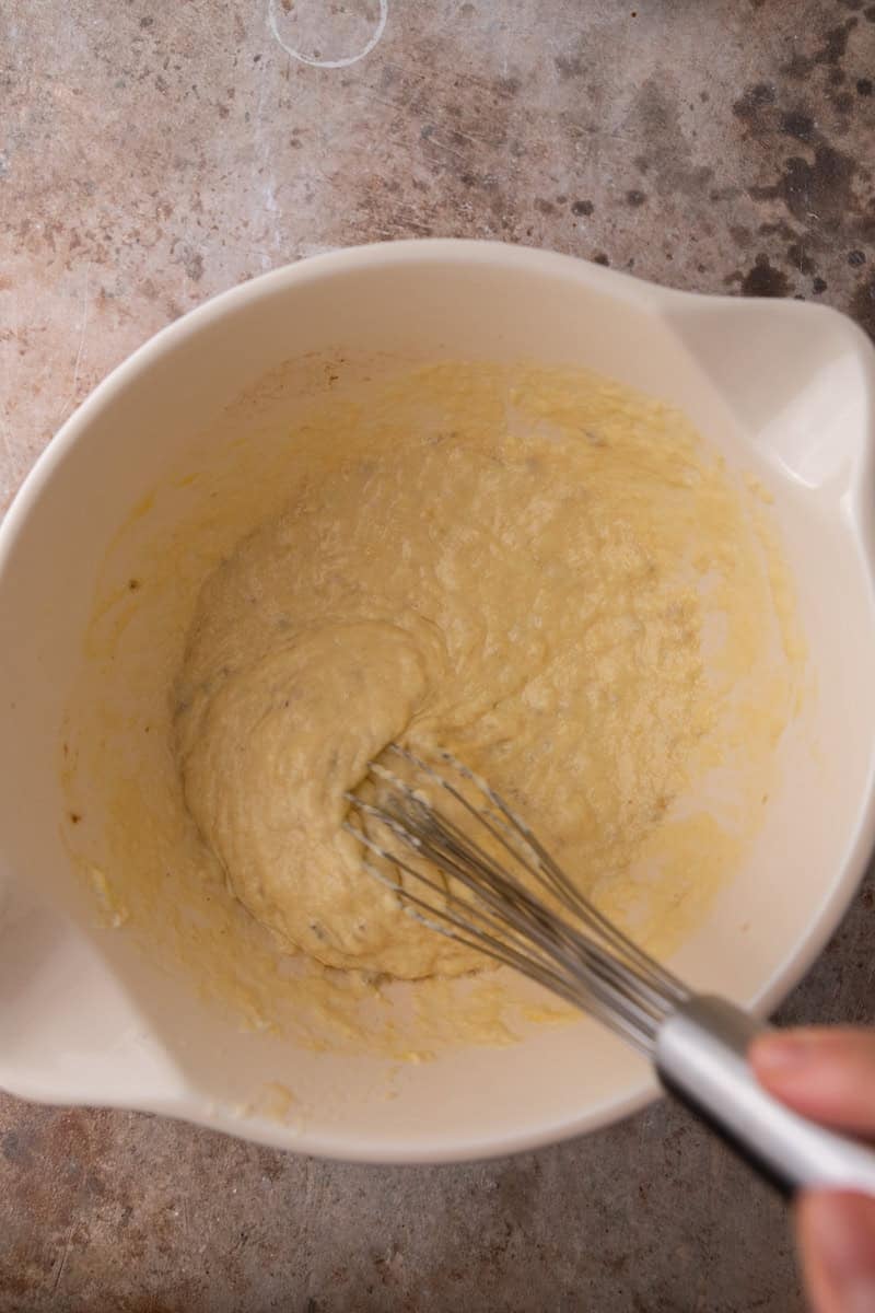 Whisking the wet banana muffin ingredients together in a white mixing bowl.