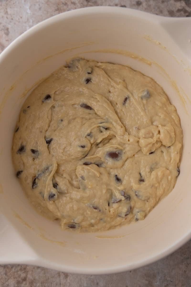 Banana muffin batter with chocolate chips folded in, resting in a white bowl.