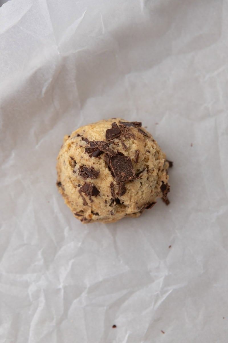 A single chilled cookie dough ball studded with chocolate on parchment paper.