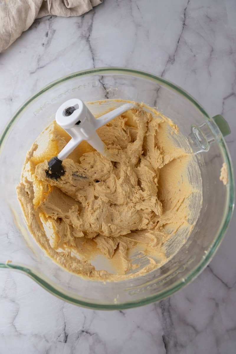 Creamed cookie dough base in a stand mixer bowl with the paddle attachment.