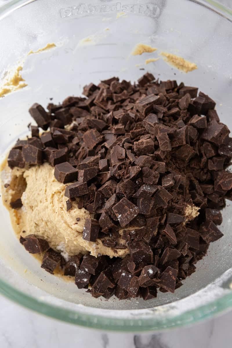 Chopped dark chocolate chunks piled on the cookie dough in a glass bowl.