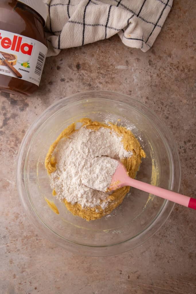 Dry ingredients added to wet cookie dough mixture in glass bowl