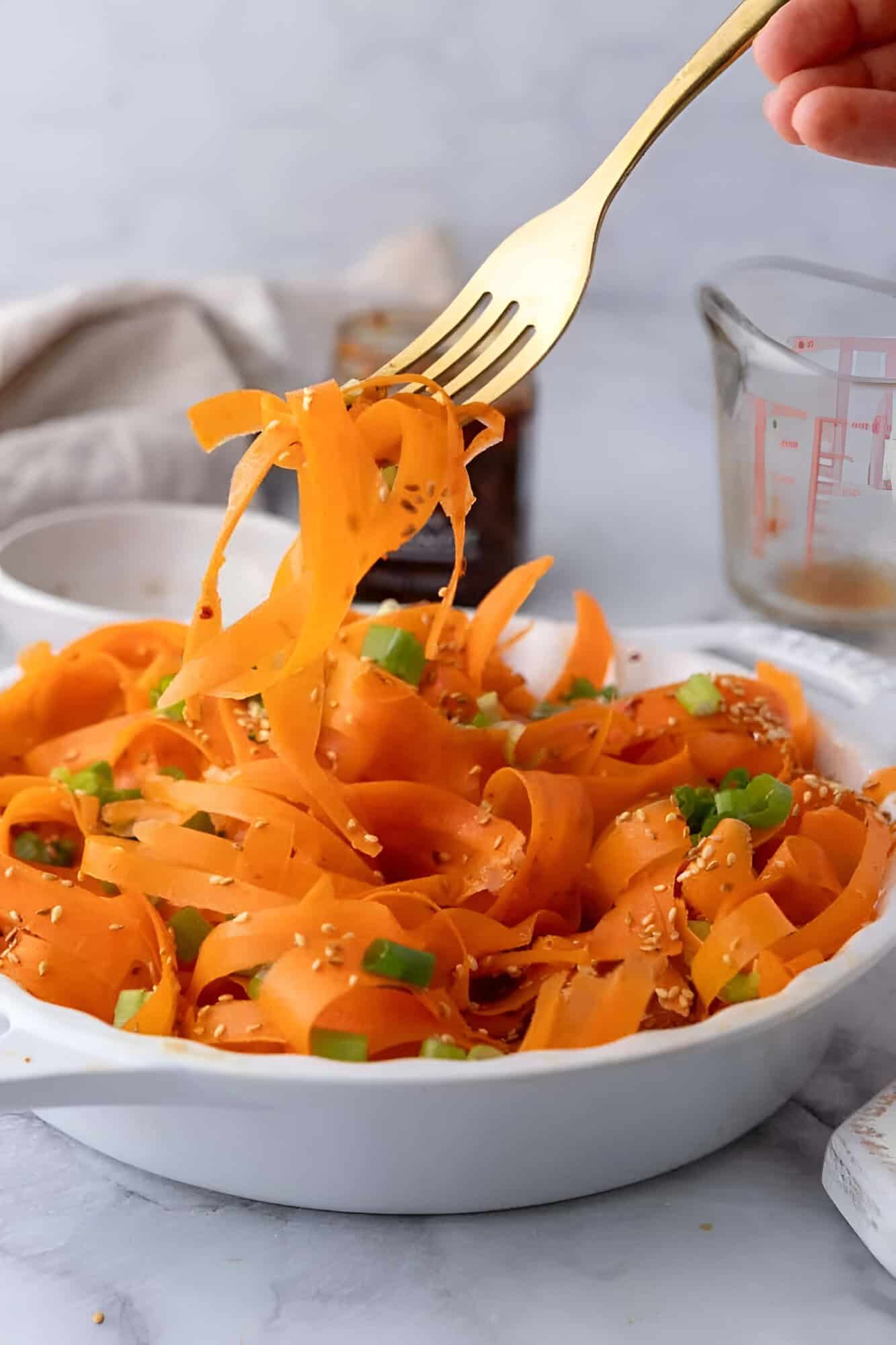Carrot ribbon salad in a white bowl topped with green onions and toasted sesame seeds.