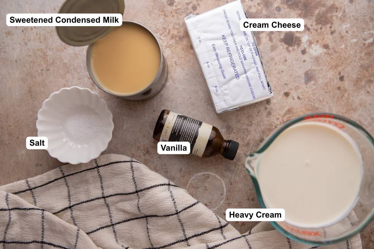 Ingredients for no-churn cream cheese ice cream on a counter, including a block of cream cheese, sweetened condensed milk, vanilla extract, heavy cream and salt.