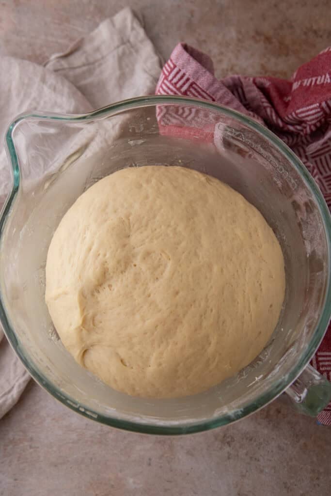 Hoagie roll dough doubled in size after the first rise in a glass mixing bowl.