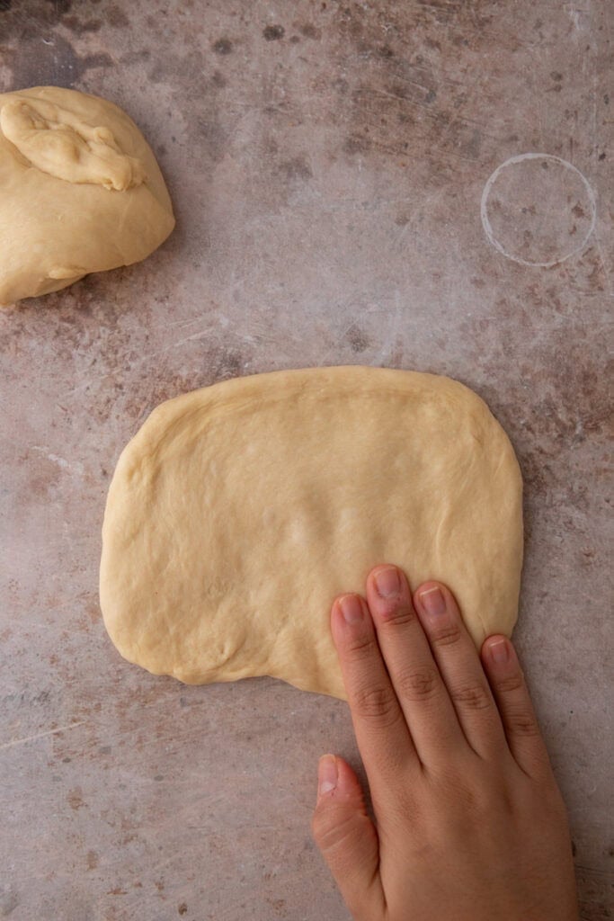 Hand pressing hoagie roll dough into a rectangle before rolling.
