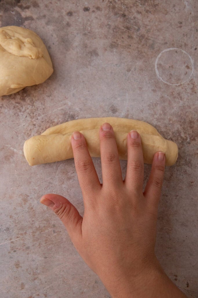 Hand rolling hoagie roll dough tightly into a log.