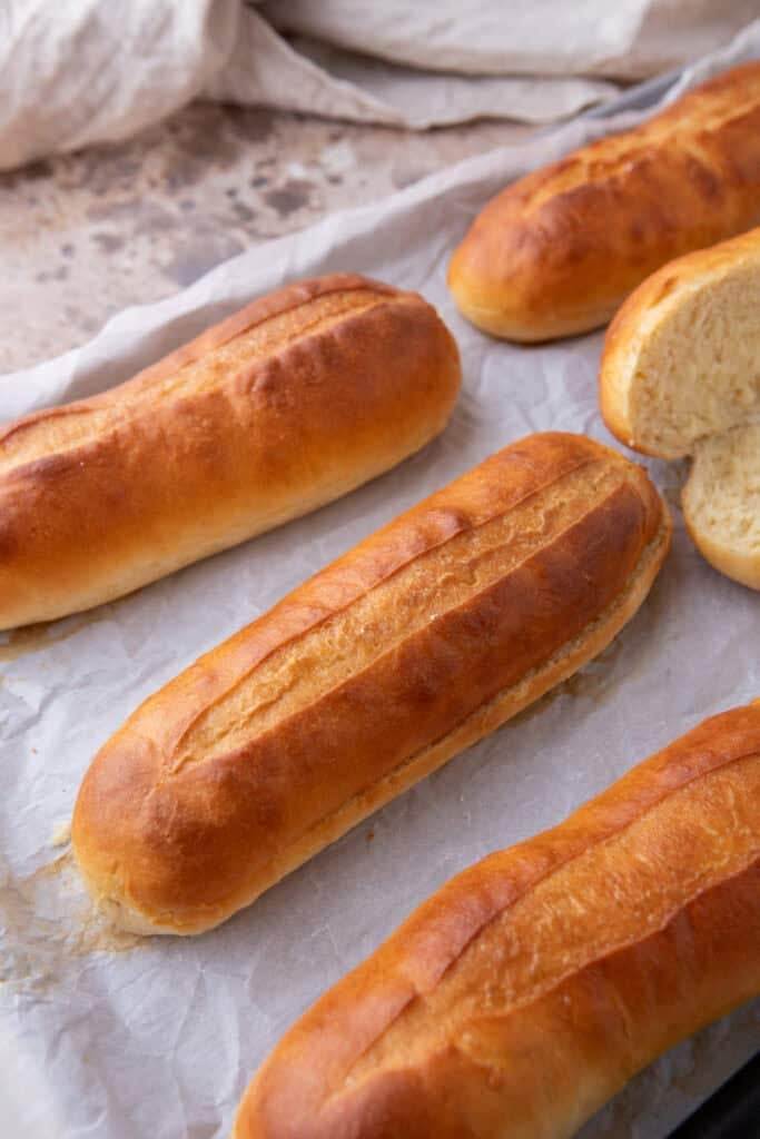 Golden baked hoagie rolls cooling on a baking sheet.