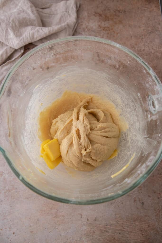 Cubed butter mixed into hoagie roll dough as it pulls away from the bowl.