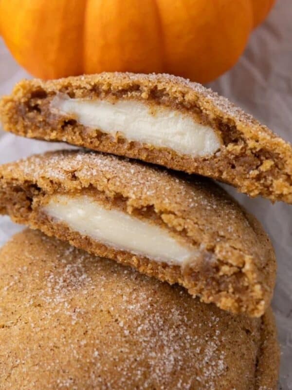 Two halves of Pumpkin Cheesecake Cookies stacked on each other, leaning on a whole cookie. Showing the inside of the cheesecake filling.