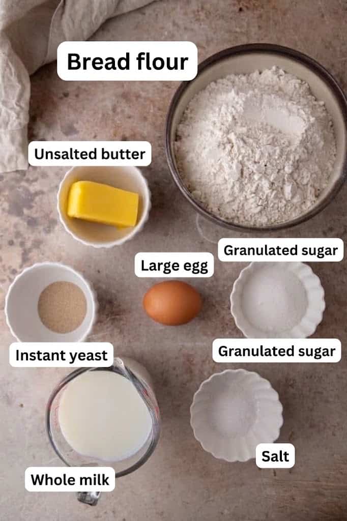 Ingredients for soft dinner rolls: bread flour, whole milk, yeast, butter, an egg, sugar, and salt.