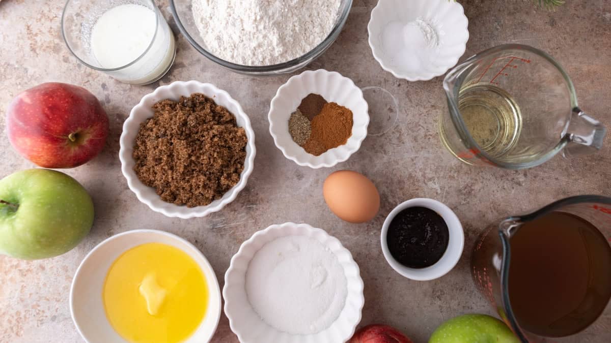 Ingredients for baked apple cider donuts, including reduced apple cider, flour, spices, sugars, egg, and butter arranged on a countertop.