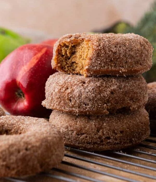 Fresh-baked apple cider donuts coated in cinnamon sugar, stacked with one donut showing a soft, fluffy inside.