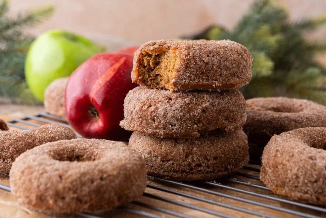 Fresh-baked apple cider donuts coated in cinnamon sugar, stacked with one donut showing a soft, fluffy inside.
