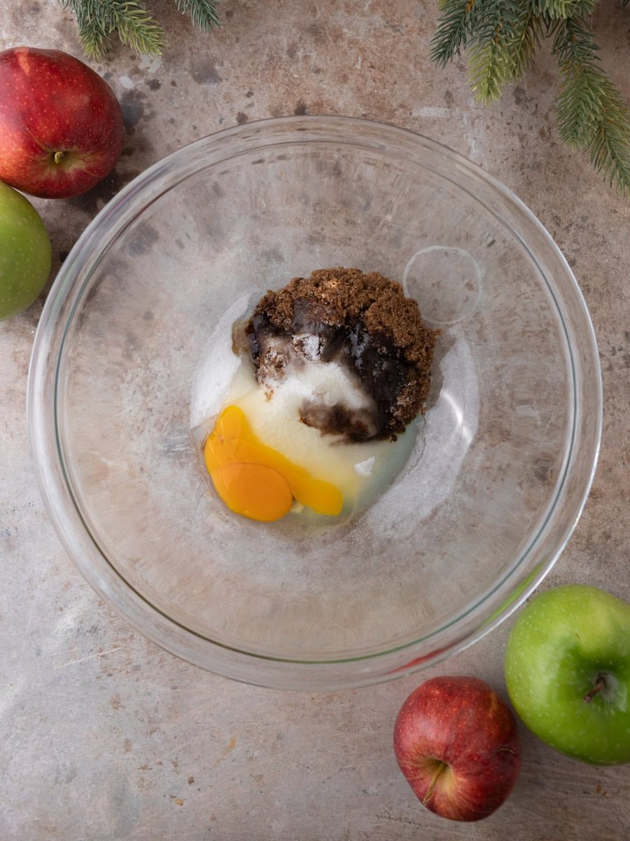 Brown sugar, granulated sugar, and egg combined in a mixing bowl for apple cider donut batter.
