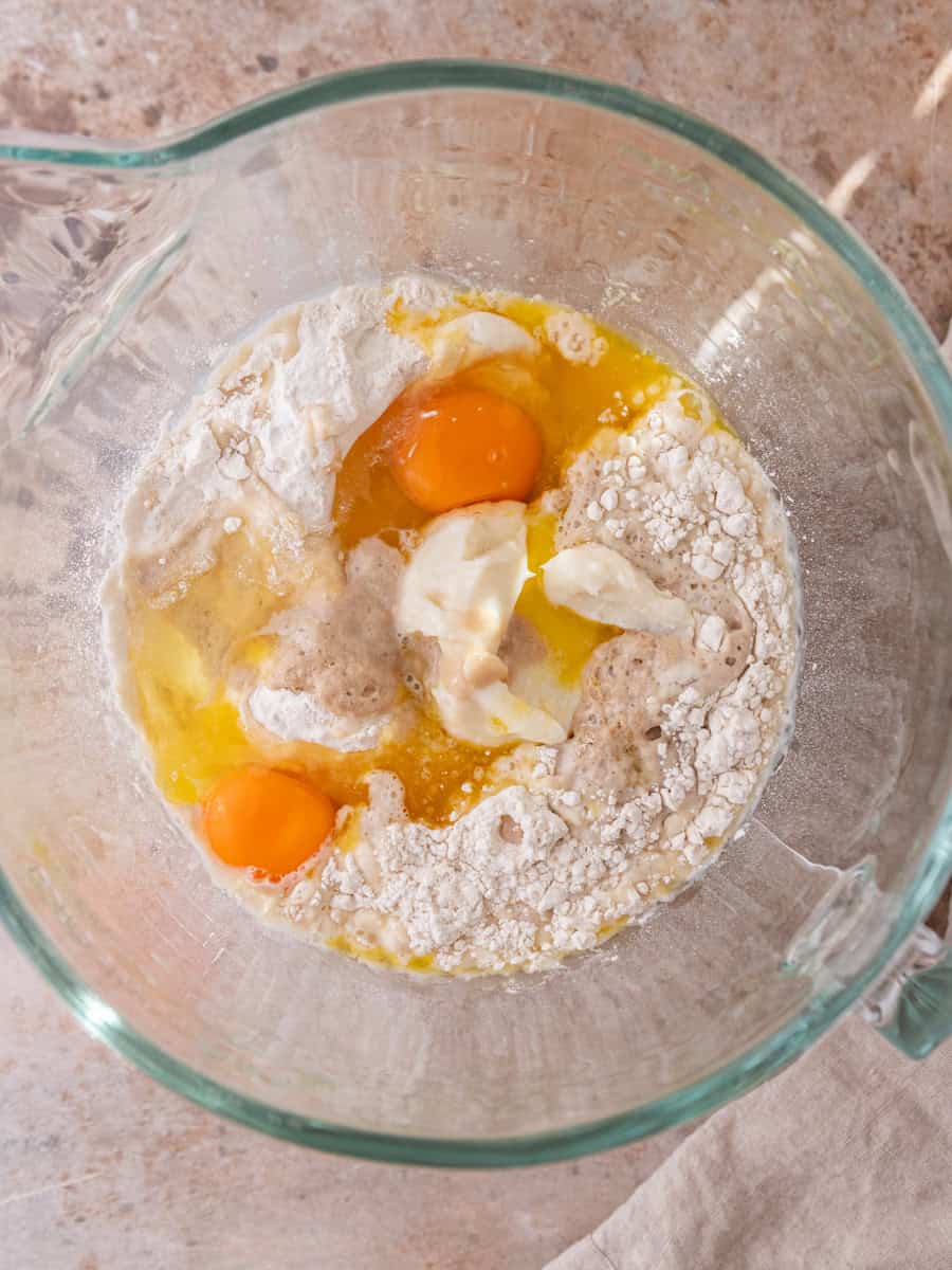 Cinnamon roll dough ingredients in mixing bowl with yeast, flour, butter, and eggs