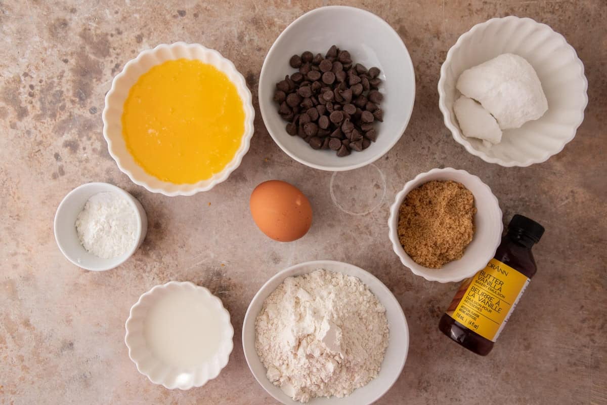 Overhead shot of ingredients for Crumbl Martha Stewart Chocolate Chip Cookies including melted butter, sugars, flour, egg, vanilla, and chocolate chips.