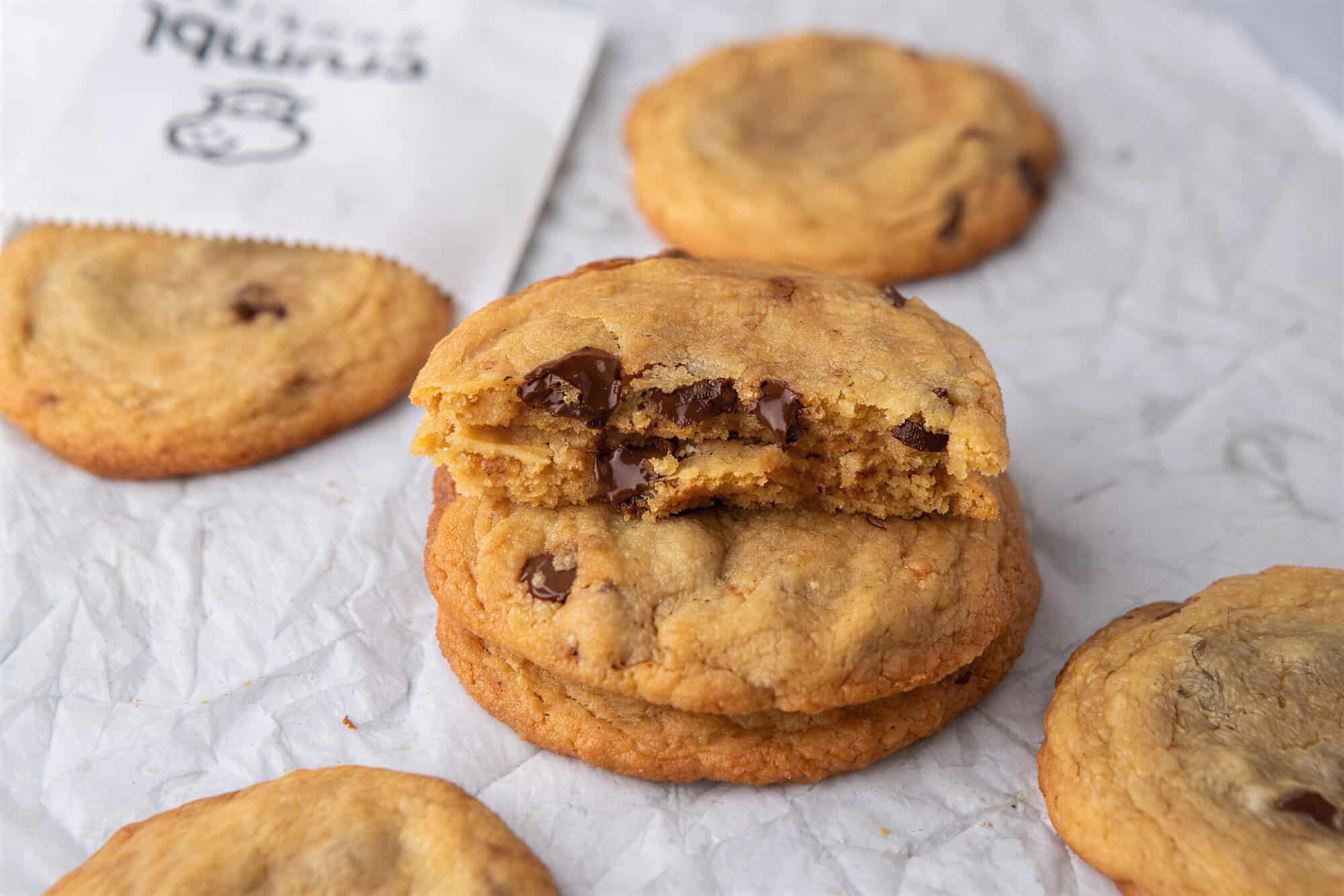 Stack of thin Crumbl-style chocolate chip cookies with melted chocolate centers and crisp golden edges.