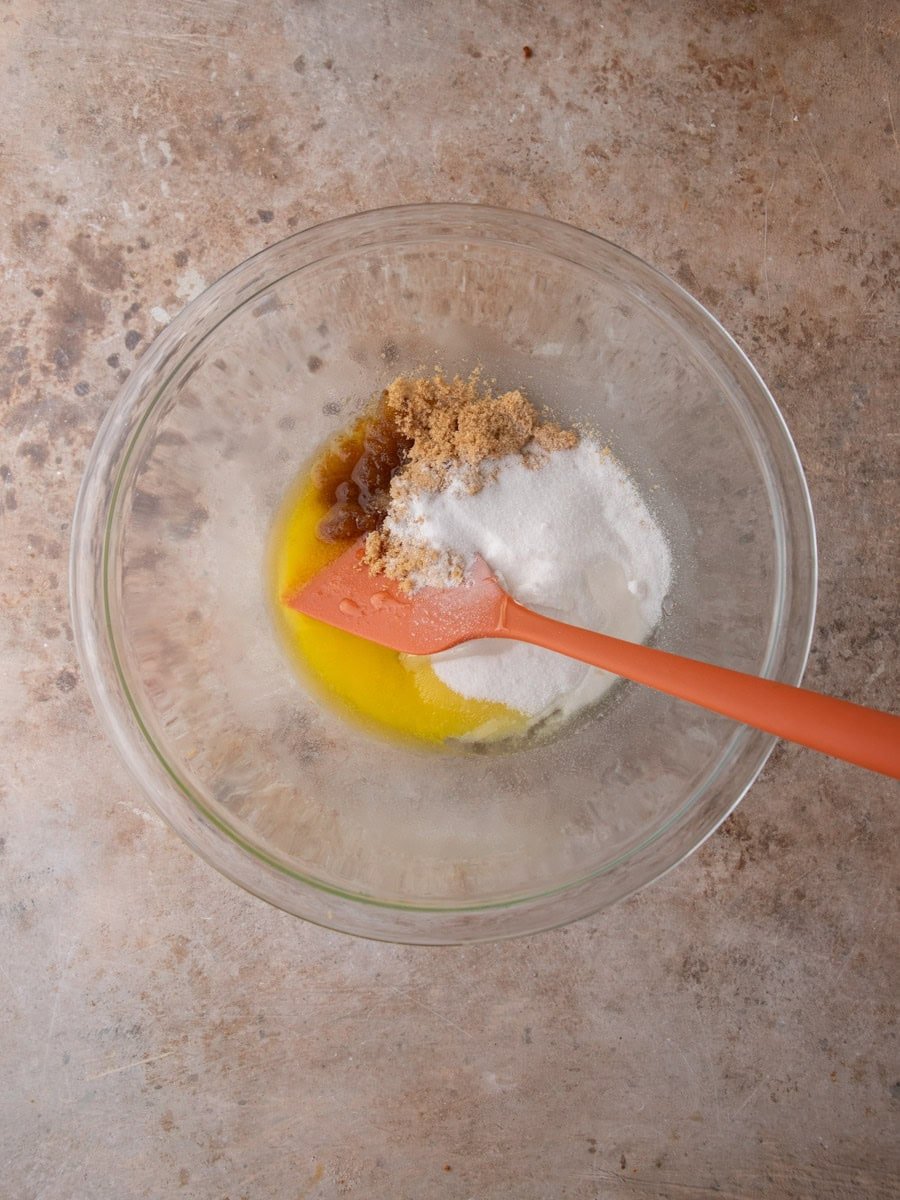 Melted butter, brown sugar, and granulated sugar combined in a glass bowl to start cookie dough.