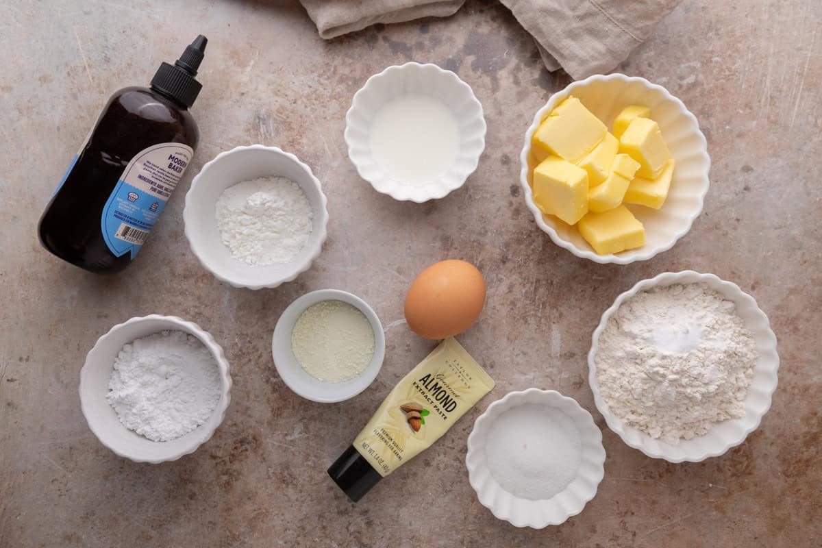 Ingredients for cookies arranged on a counter, including butter, flour, sugar, egg, and extracts.
