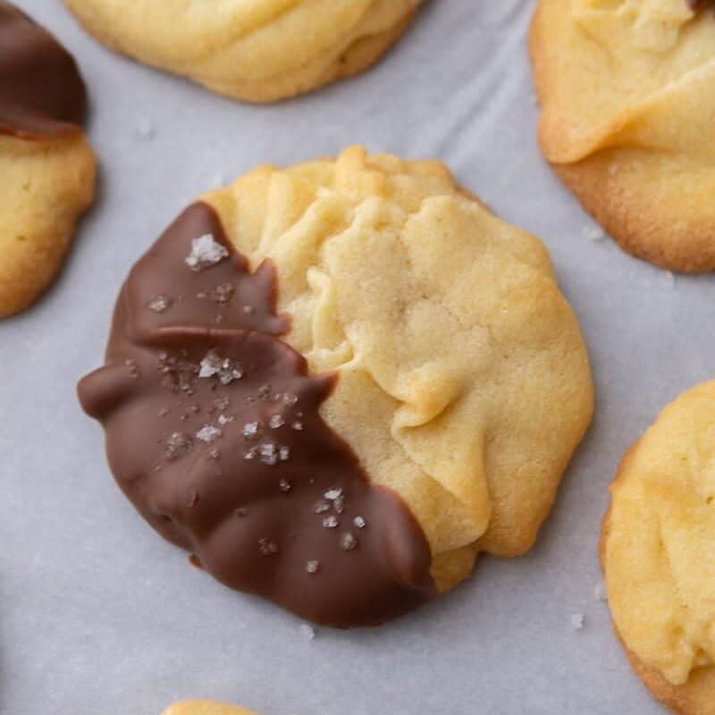 Close-up of a Danish butter cookie partially dipped in chocolate and sprinkled with flaky salt.