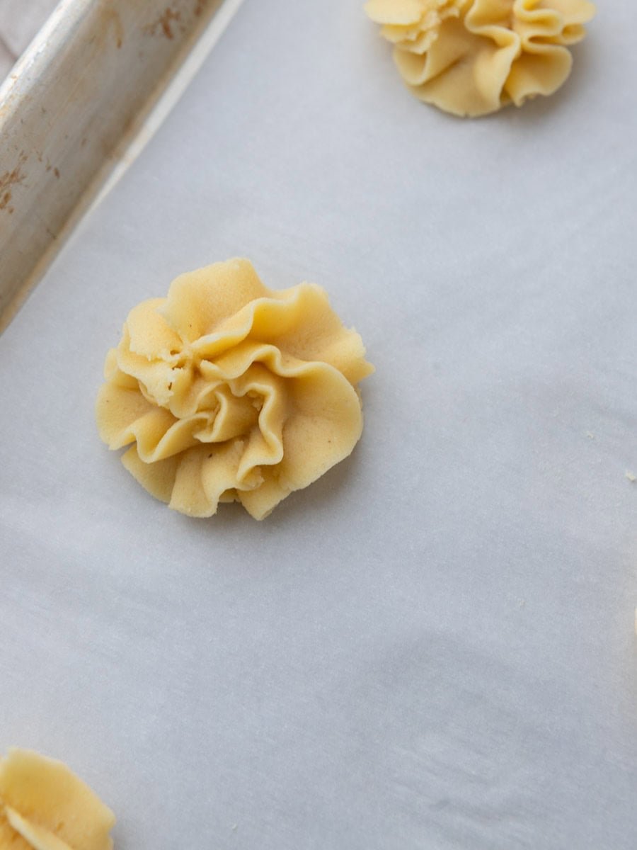 Unbaked piped butter cookie rosette on a parchment-lined baking sheet.
