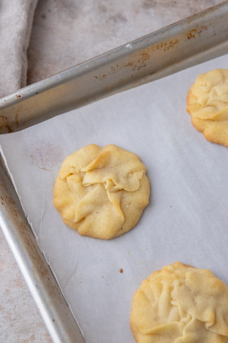 Freshly baked Danish butter cookie cooling on a parchment-lined baking sheet.
