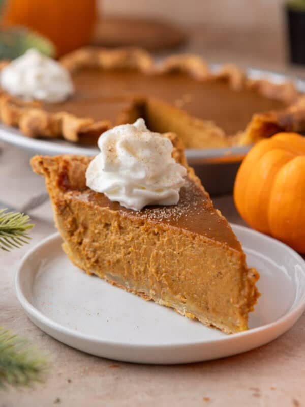 A thick slice of homemade pumpkin pie topped with a swirl of whipped cream and dusted with cinnamon on a white plate.