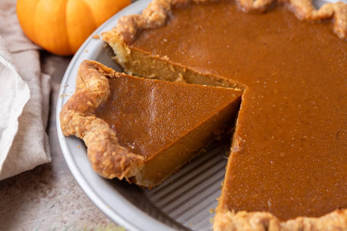 Homemade pumpkin pie with a flaky golden crust and smooth pumpkin filling with one slice cut out, showing its creamy texture.