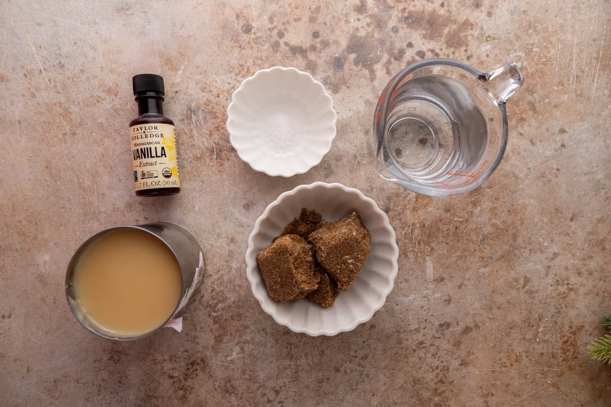 Ingredients on the counter. Dark brown sugar, sweetened condensed milk, vanilla extract, salt, and water arranged on a countertop.