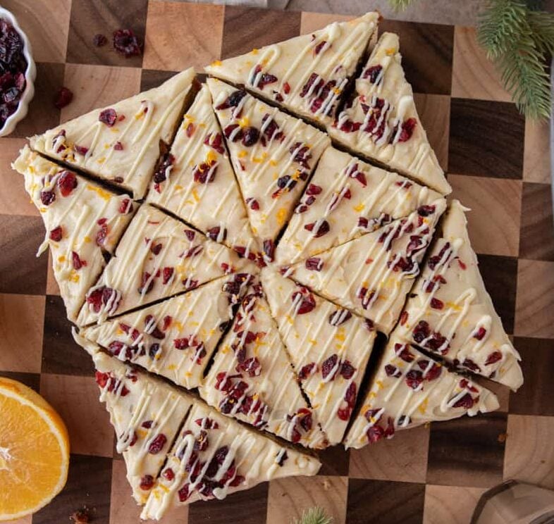 Overhead view of frosted cranberry bliss bars cut into triangles and arranged neatly on a wooden board.