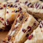 Close-up of Starbucks cranberry bliss bars showing layers of chewy blondie, white chocolate chunks, and cream cheese frosting topped with dried cranberries and orange zest.