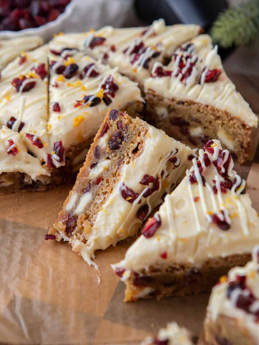 Copycat Starbucks cranberry bliss bars sliced into triangles on parchment paper showing the chewy blondie base with cream cheese frosting, dried cranberries, and orange zest on top
