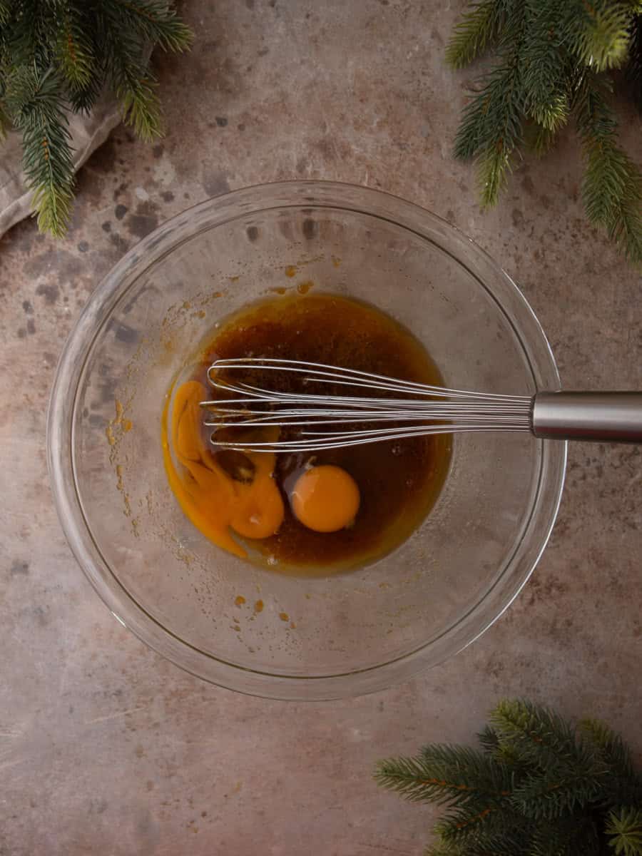 Eggs added to the melted butter and brown sugar mixture in a glass bowl with a whisk.