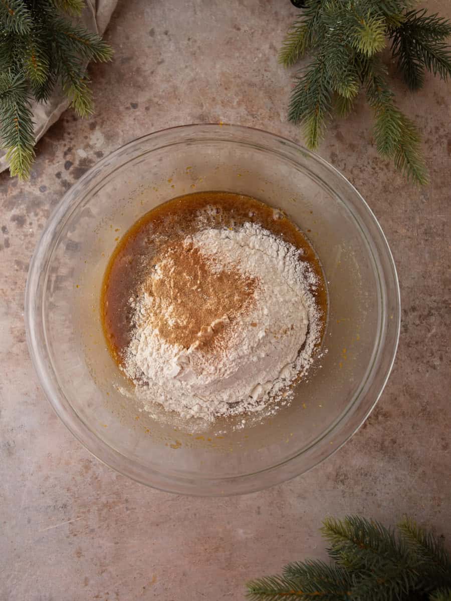 Flour and warm spices sitting on top of wet batter in a glass mixing bowl before folding.
