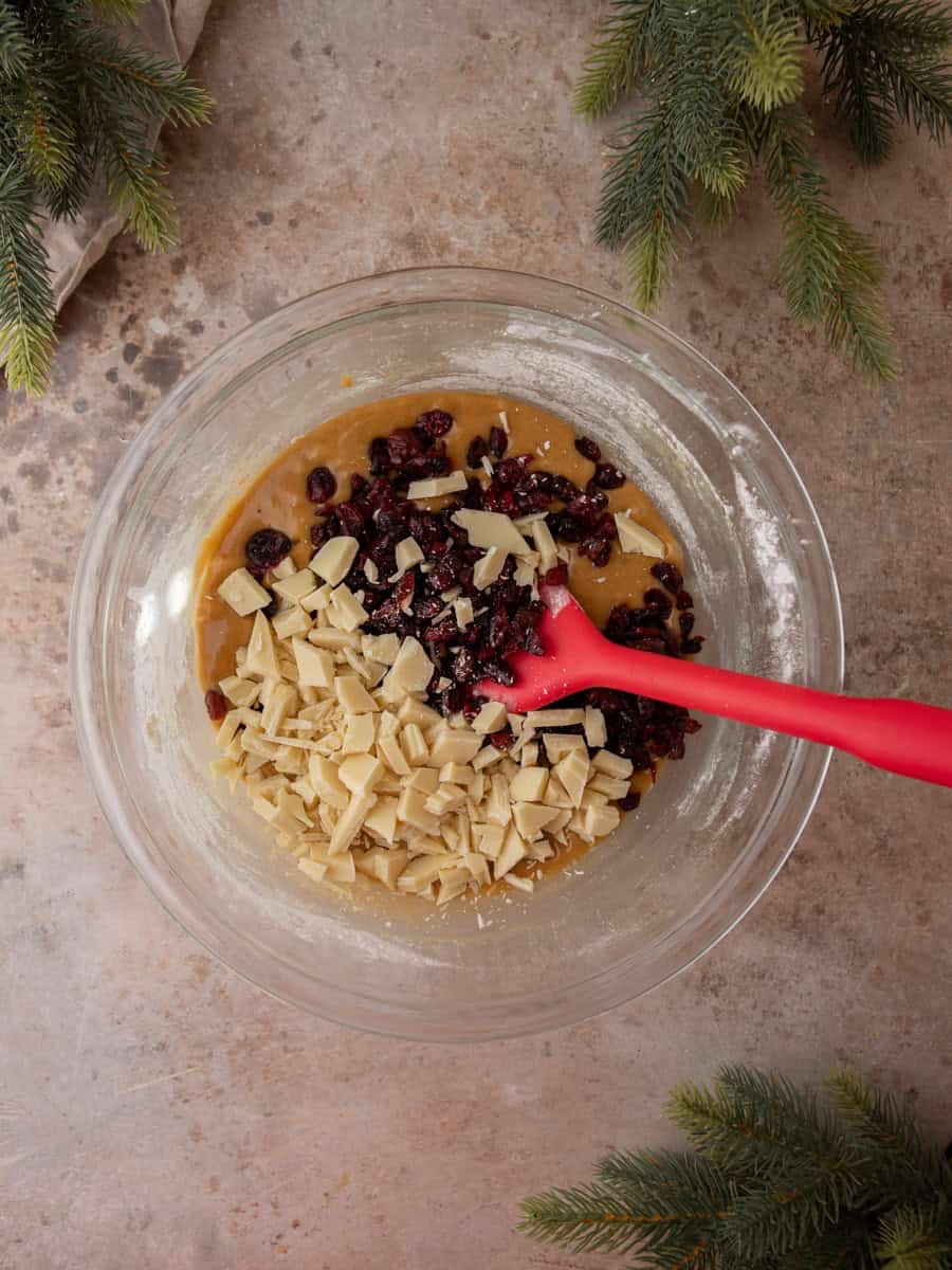 Blondie batter mixed with dried cranberries and chopped white chocolate in a glass bowl.