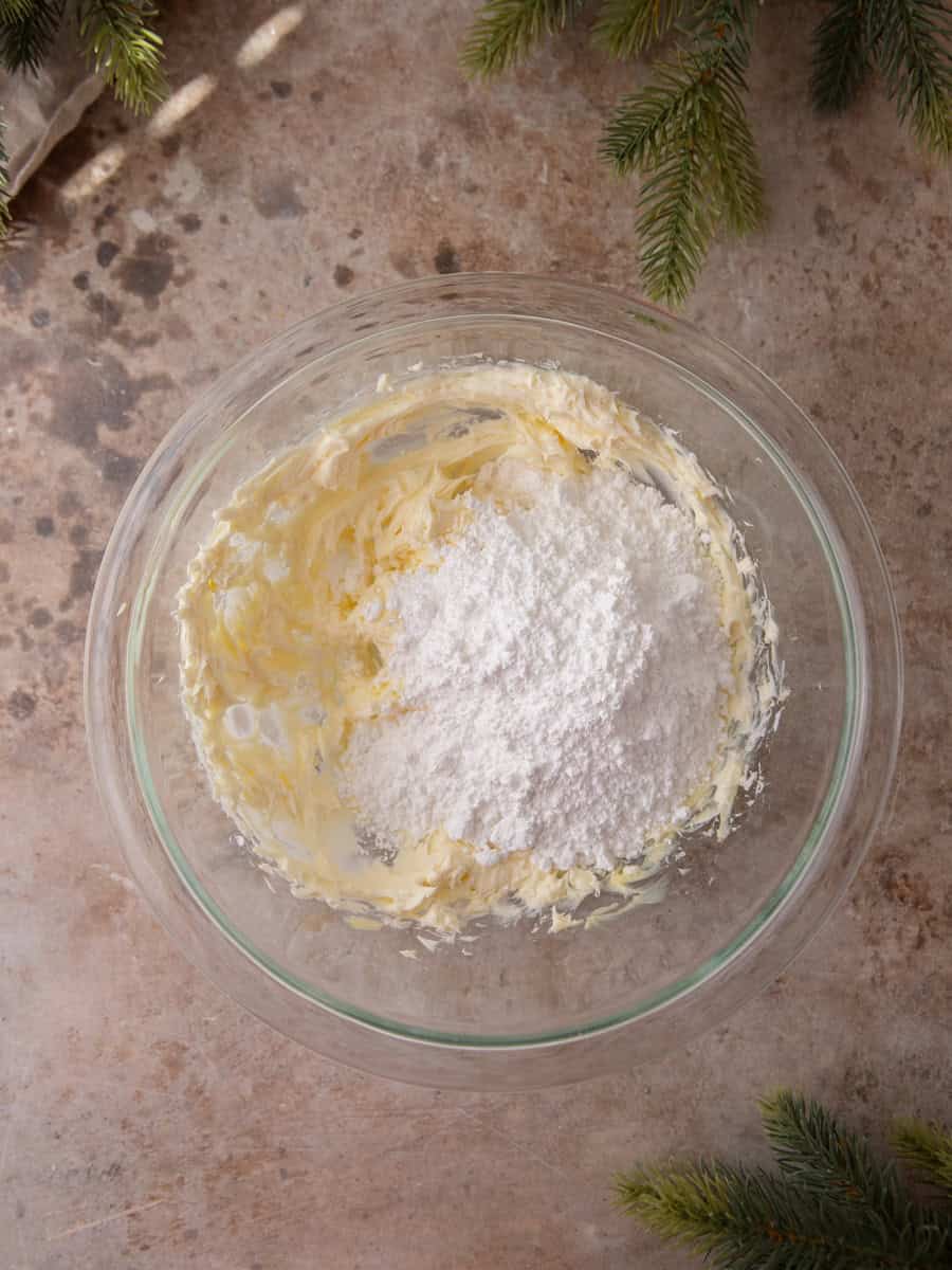 Cream cheese and powdered sugar being mixed in a glass bowl to make frosting.