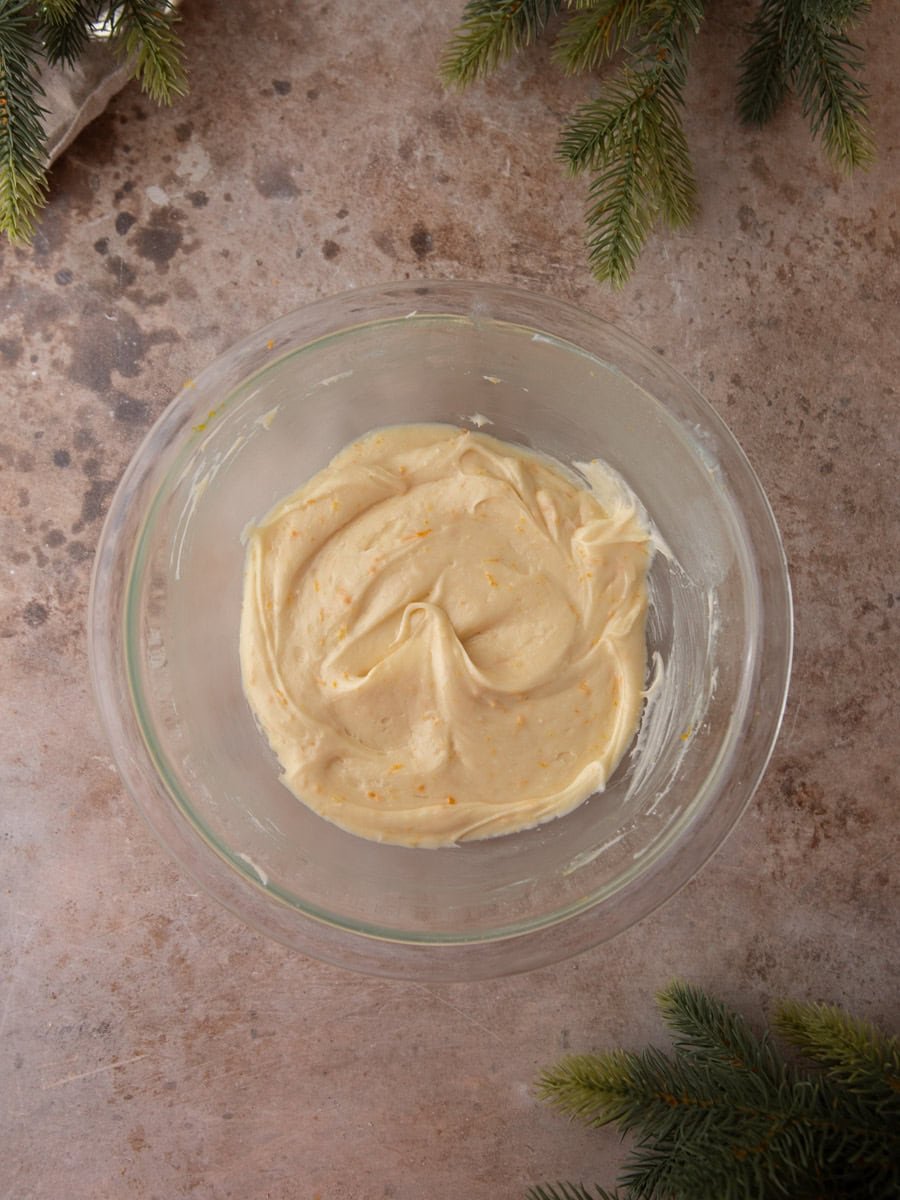 Creamy orange-speckled frosting in a glass bowl on a stone countertop.