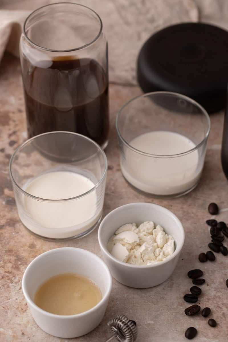 Ingredients, including cold brew, heavy cream, milk, vanilla syrup, and whey protein powder on a counter.