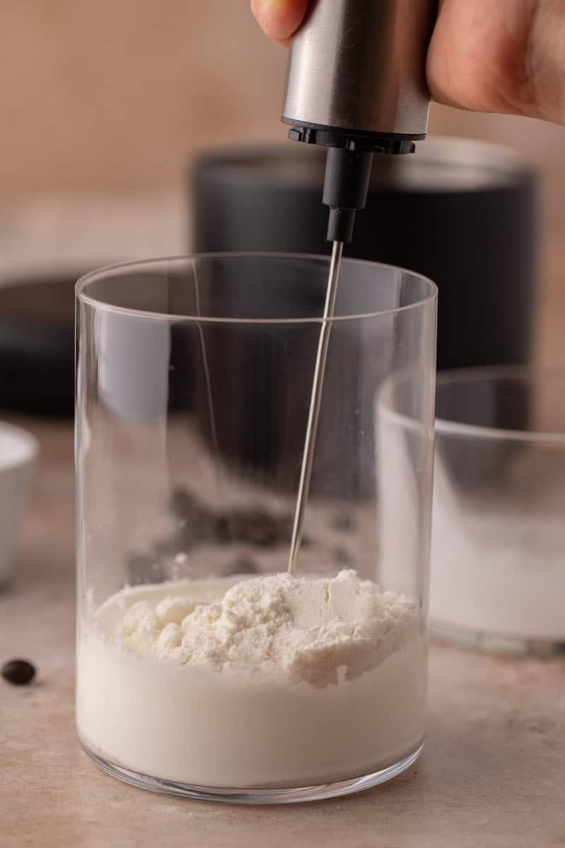 Handheld frother mixing cream and protein powder.