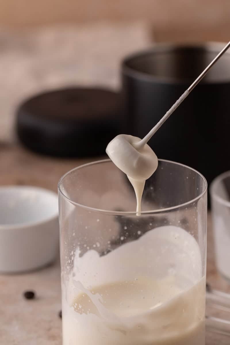 Thick cold foam drizzling off a frother whisk to show creamy texture.