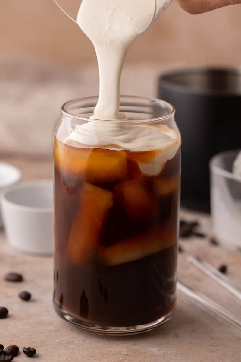 Thick homemade protein cold foam being poured over iced coffee.
