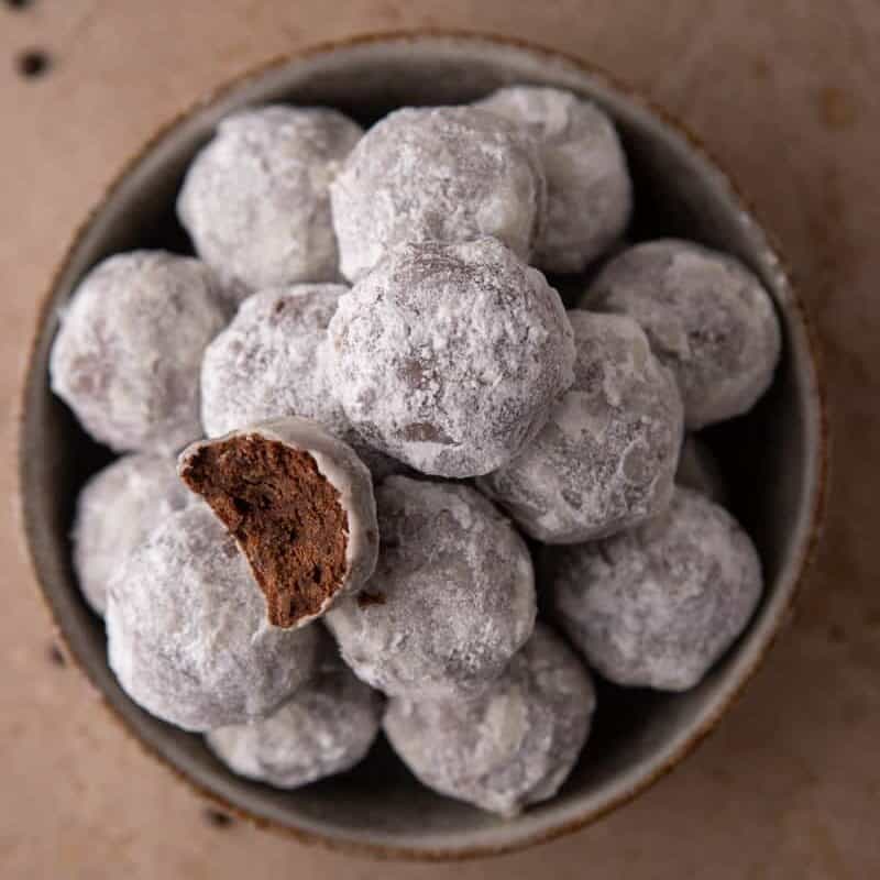 Bowl of powdered sugar–coated chocolate cookies with one cookie broken open.