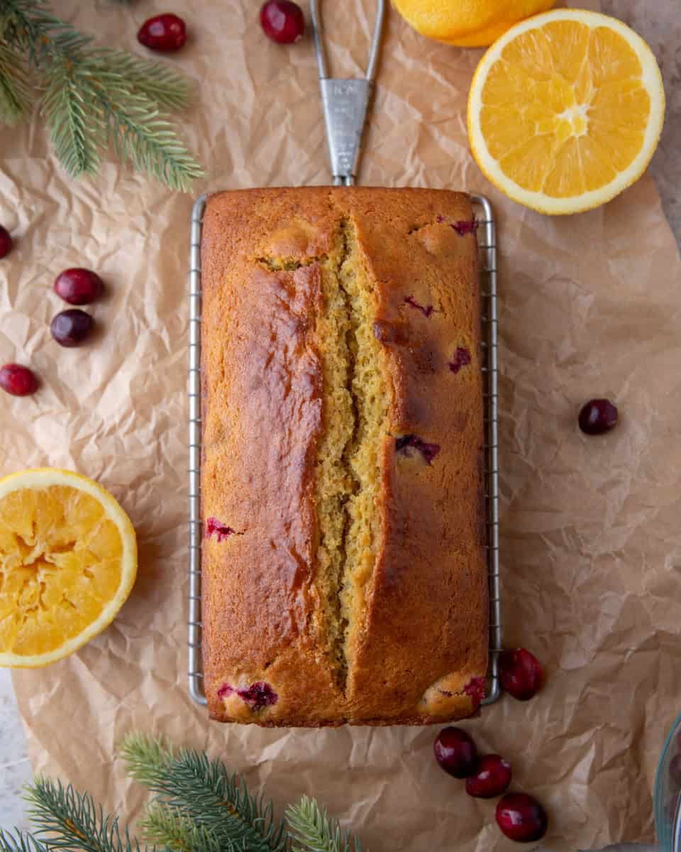 Baked cranberry orange bread cooling on a wire rack with fresh oranges and cranberries