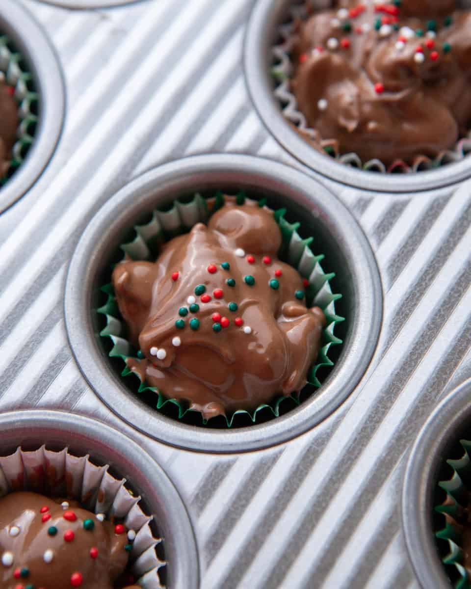 Crockpot candy clusters portioned into mini cupcake liners with Christmas sprinkles